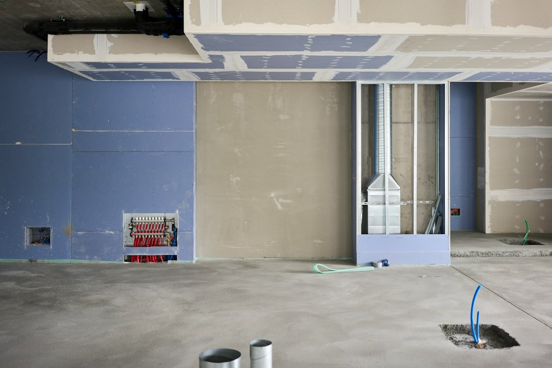 Commercial interior fit-out in progress with taped drywall on walls and ceiling, an open stud bay with ductwork and a bare concrete floor