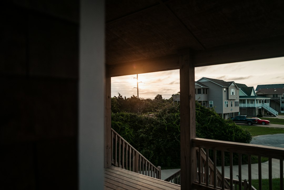 View from a shaded wooden porch toward suburban houses and a parked truck at sunset