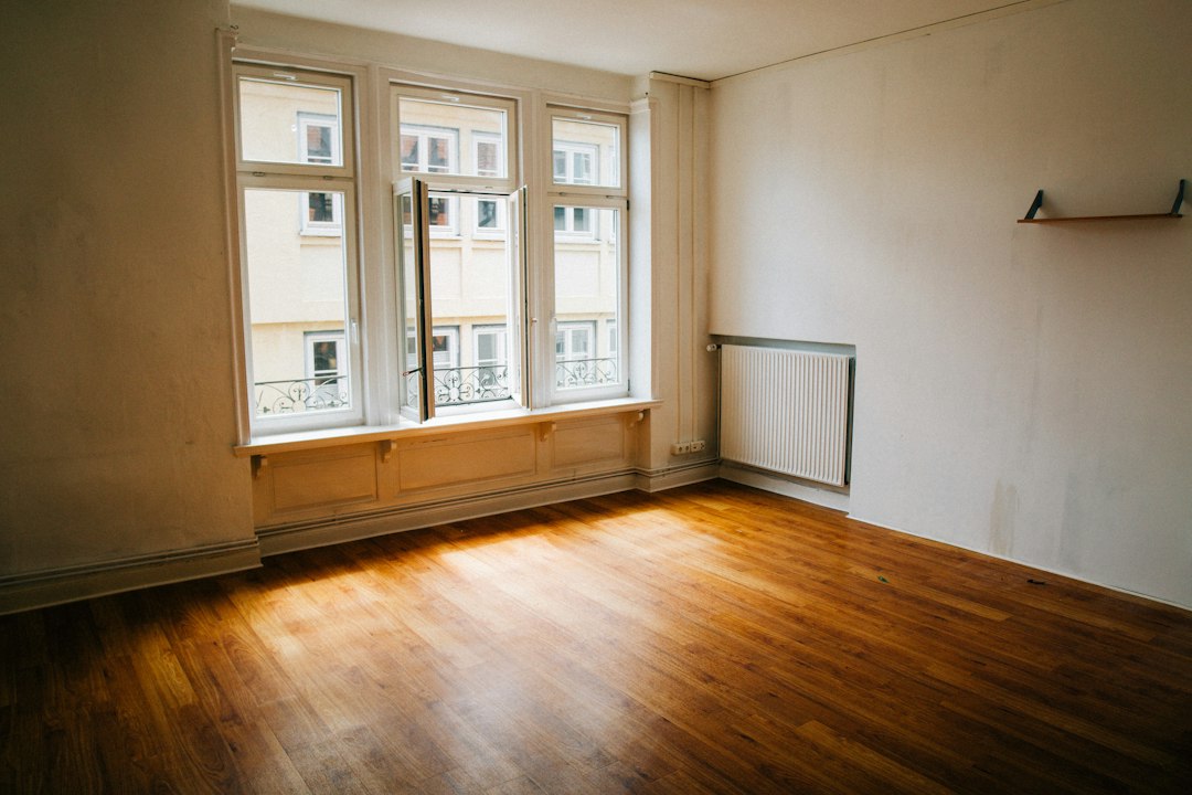 Empty apartment with bare walls, a radiator and sunlight on a wood floor between tenants