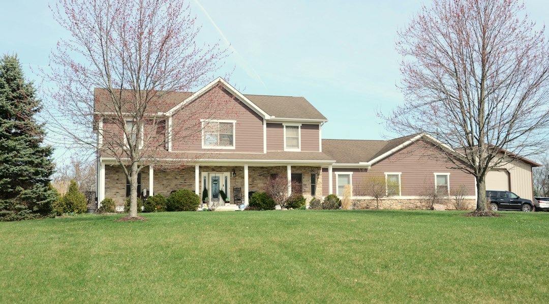 Two-story suburban house with a stone front porch, siding and an attached garage behind a wide spring lawn