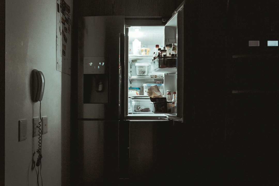 Open side-by-side stainless refrigerator lit from inside in a dark kitchen