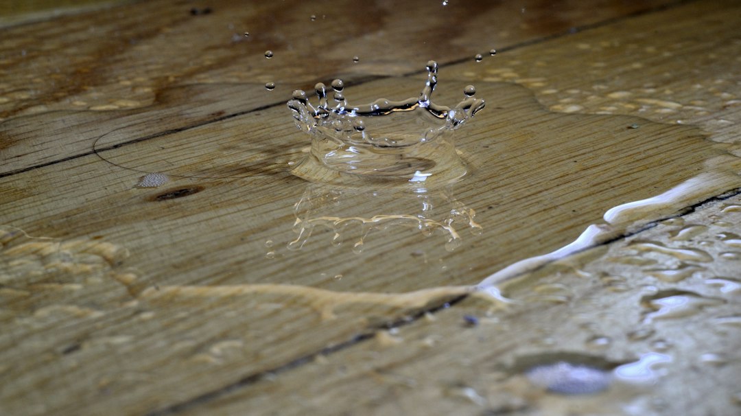 Water dripping into a puddle spreading across wooden floor planks